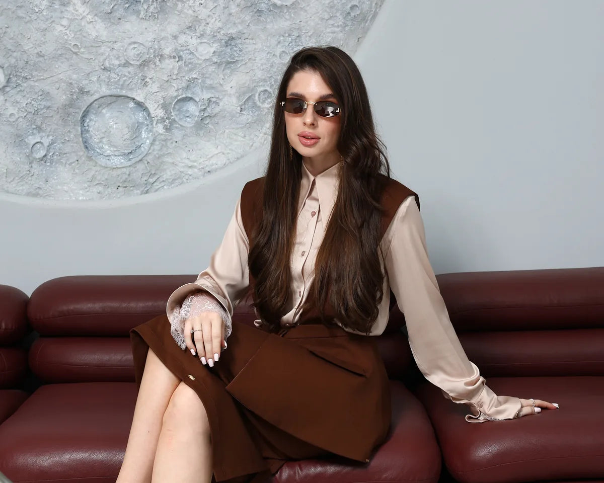 The DIID Contessa Set, a chocolate-brown waistcoat and skirt with a champagne satin shirt, styled seated by a chess table