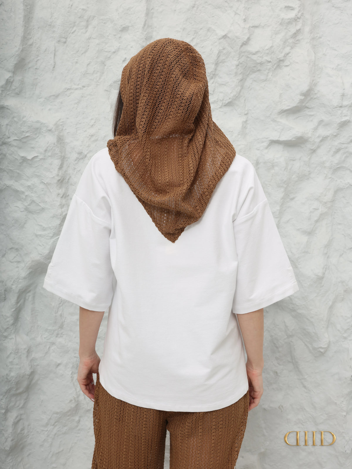 Back view of the brown crochet-knit hood draping down the white top